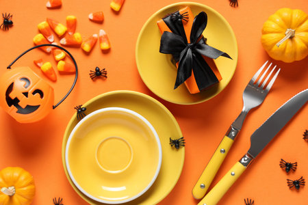 Festive table setting for Halloween celebration with gift box, candies and pumpkins on orange...