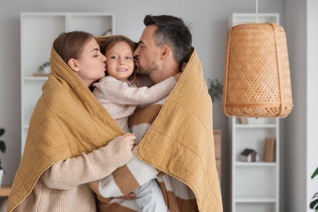 Parents with warm plaid kissing their little daughter at homeの写真素材