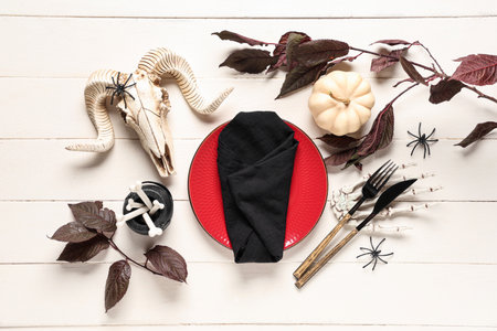 Festive table setting for Halloween celebration with sheep skull, autumn leaves and skeleton hand on white wooden backgroundの写真素材