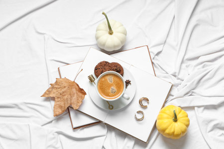 Cup of tasty pumpkin coffee with cookies, autumn decorations, books and jewelery on bed at homeの写真素材