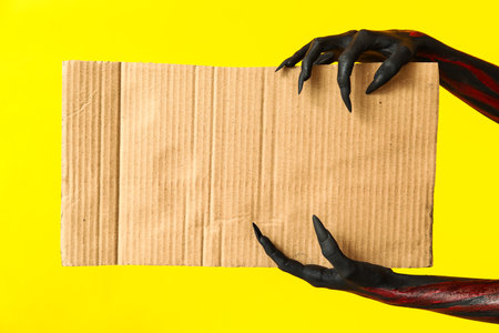 Black witch hands with claws and piece of cardton on yellow background. Halloween celebrationの写真素材