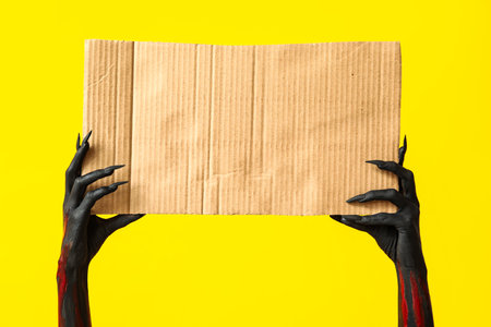Black witch hands with claws and piece of cardton on yellow background. Halloween celebrationの写真素材