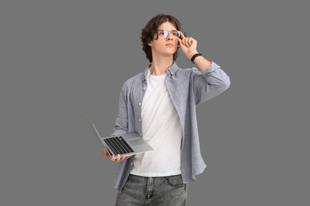 Male programmer in eyeglasses with modern laptop on gray background