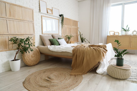 Beautiful interior of bedroom with cozy bed, pouf, houseplants and rugの写真素材