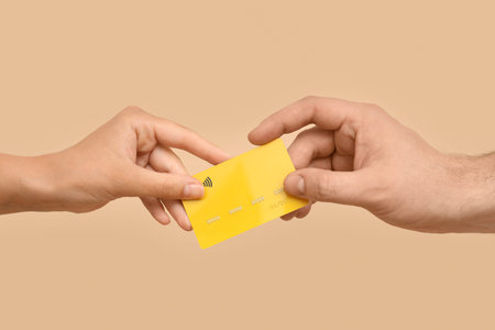 Hands of loving young couple with credit card on beige background