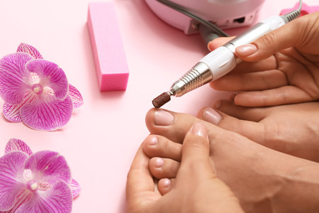 Young woman with beautiful pedicure using milling cutter on pink background, closeupの写真素材