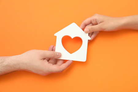 Loving young couple with figure of house holding hands on orange backgroundの写真素材