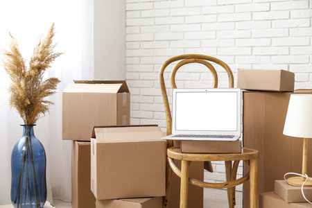 Blank laptop on chair with moving boxes and pampas grass in light room