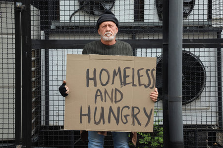 Mature man holding cardboard with text HOMELESS AND HUNGRY on street