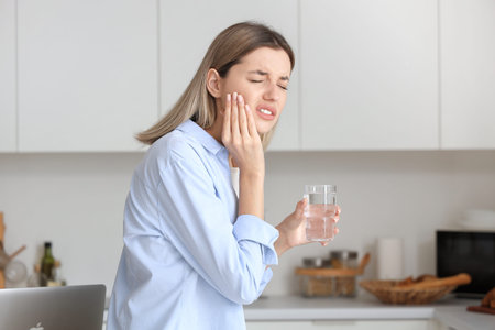 Young woman with glass of cold water suffering from tooth ache at homeの写真素材
