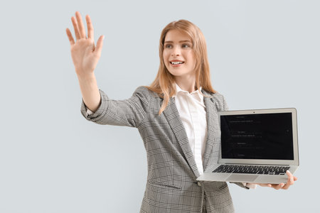 Young businesswoman with laptop using virtual screen on gray backgroundの写真素材