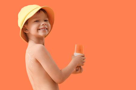 Cute little boy with sunscreen cream on orange backgroundの写真素材