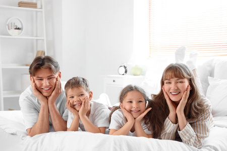Happy parents with their little children lying in bedroomの写真素材