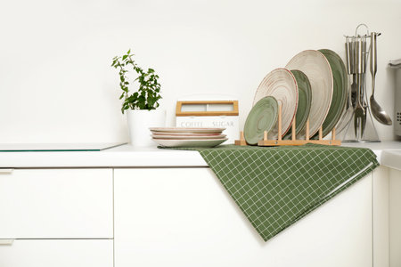 Stacks of different clean plates near houseplant on white counter in kitchenの写真素材