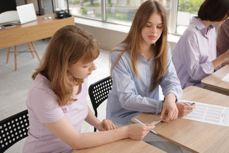 Female student handing cheat sheet over during exam in classroomの写真素材