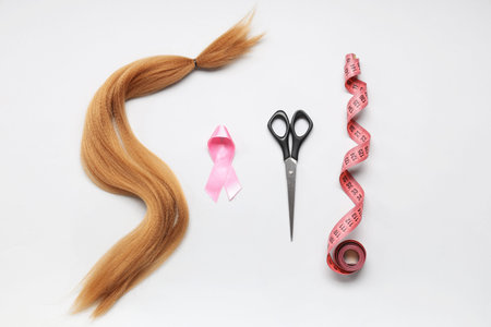 Red hair strand for donation with scissors, pink awareness ribbon and measuring tape on white...