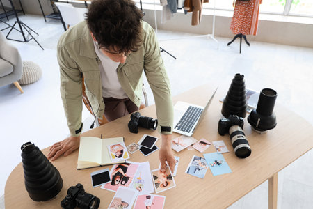 Professional male photographer with modern cameras choosing photos on table in studioの写真素材