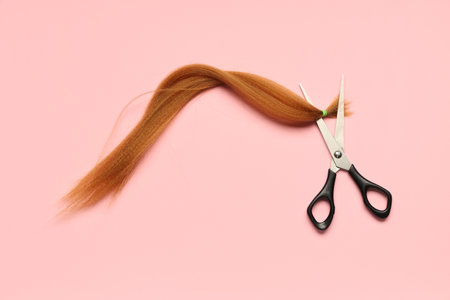 Red hair strand for donation with scissors on pink backgroundの写真素材