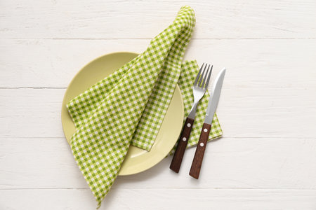 Table setting with plate, cutlery and checkered napkins on beige wooden backgroundの写真素材