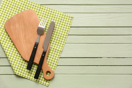 Table setting with board, cutlery and napkin on green wooden backgroundの写真素材