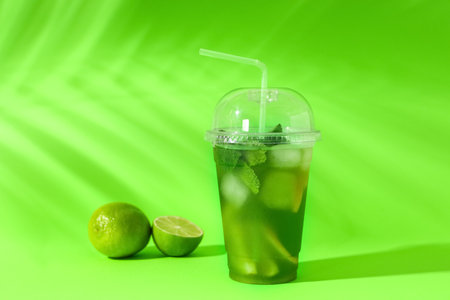 Plastic cup of tasty lemonade with limes on green backgroundの写真素材