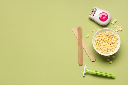 Modern epilator with razor, wax and sticks on green background
