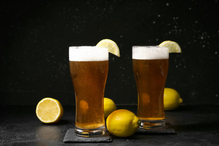 Glasses of fresh beer with lemons on black background