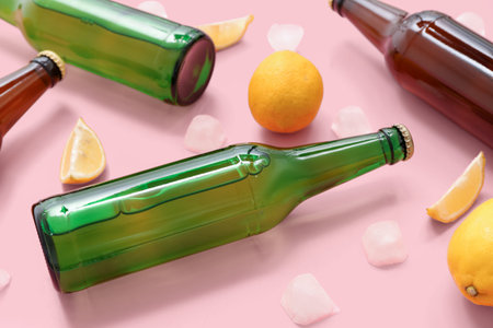 Bottles of fresh beer with lemon and ice cubes on pink background