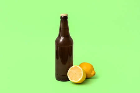Bottle of fresh beer with lemon on green background