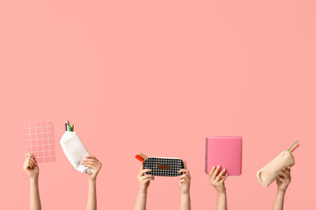 Female hands holding notebooks and pencil cases with stationery on pink backgroundの写真素材