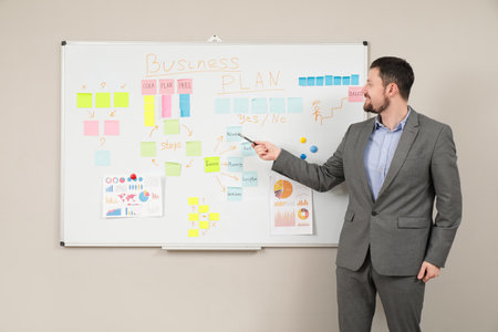 Young man near whiteboard with business plan on light wallの写真素材