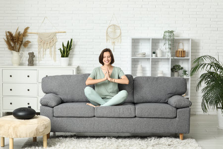 Young woman meditating while sitting on sofa at homeの写真素材