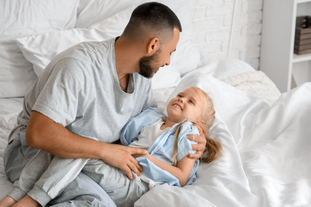Father tickling his little daughter in bedroomの写真素材