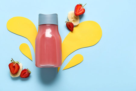 Sports bottle of fresh strawberry juice with banana and splashes made of paper on blue backgroundの写真素材