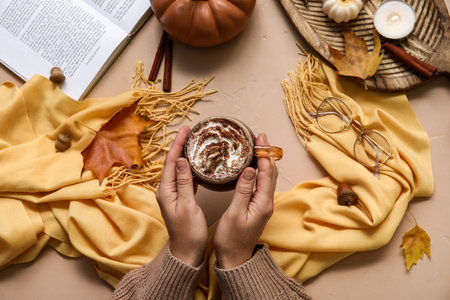 Female hands with cup of cocoa and scarf on beige backgroundの写真素材