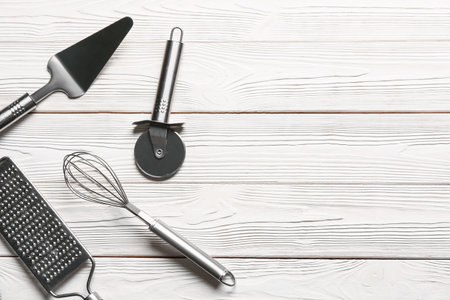 Set of stainless steel kitchen utensils with pizza cutter on white wooden background