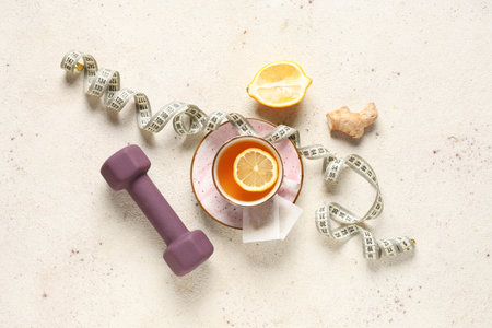 Cup of tea for weight loss, dumbbell and measuring tape on white grunge tableの写真素材