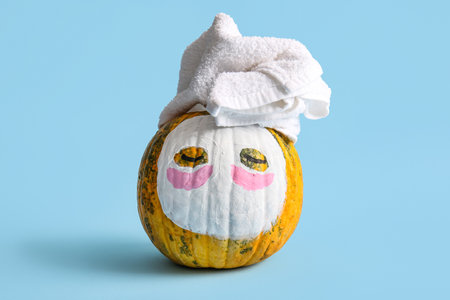 Pumpkin with drawn face, towel and cosmetic mask on color backgroundの写真素材