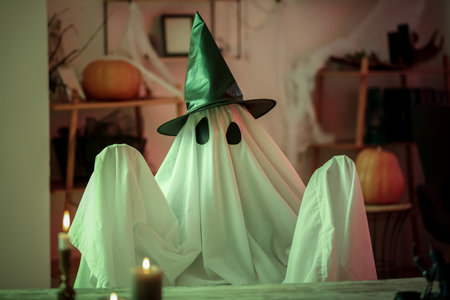 Person in Halloween costume of ghost with witch hat and burning candles at homeの写真素材