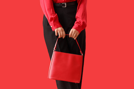 Beautiful young woman in autumn outfit with stylish bag on red background, closeupの写真素材