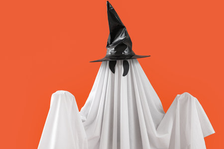 Person in Halloween costume of ghost and witch hat on orange backgroundの写真素材