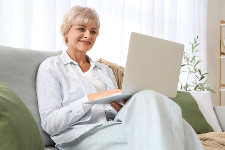 Mature woman using laptop on sofa at homeの写真素材