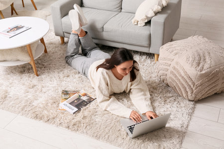 Young woman using laptop on carpet at homeの写真素材