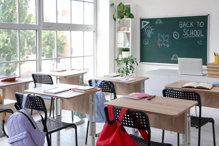 Interior of empty classroom with school desks and text BACK TO SCHOOL on chalkboard