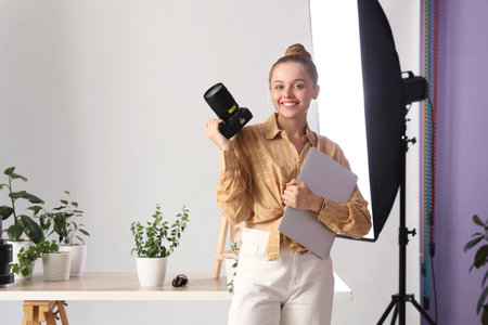 Female photographer with camera and laptop near plants on table in photo studioの写真素材