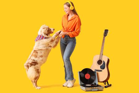 Young woman in headphones dancing with Australian Shepherd dog and record player on yellow backgroundの写真素材