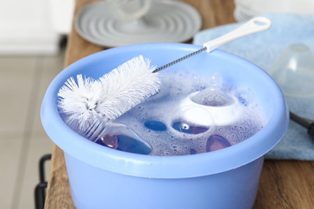 Basin of water with cleaning brush and baby bottles on counter in kitchen, closeupの写真素材