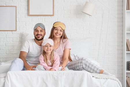 Happy parents and their little daughters with sleeping masks sitting in bedroomの写真素材