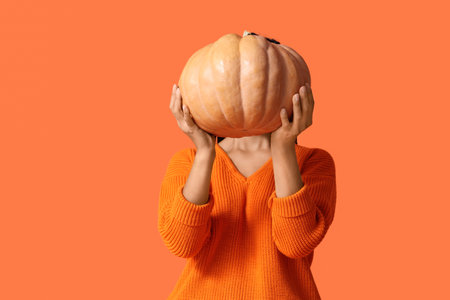Beautiful young African-American woman with pumpkin on orange backgroundの写真素材