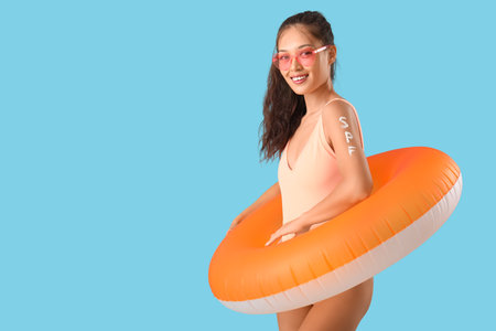 Young Asian woman in swimsuit with word SPF made of sunscreen cream and swim ring on blue backgroundの写真素材